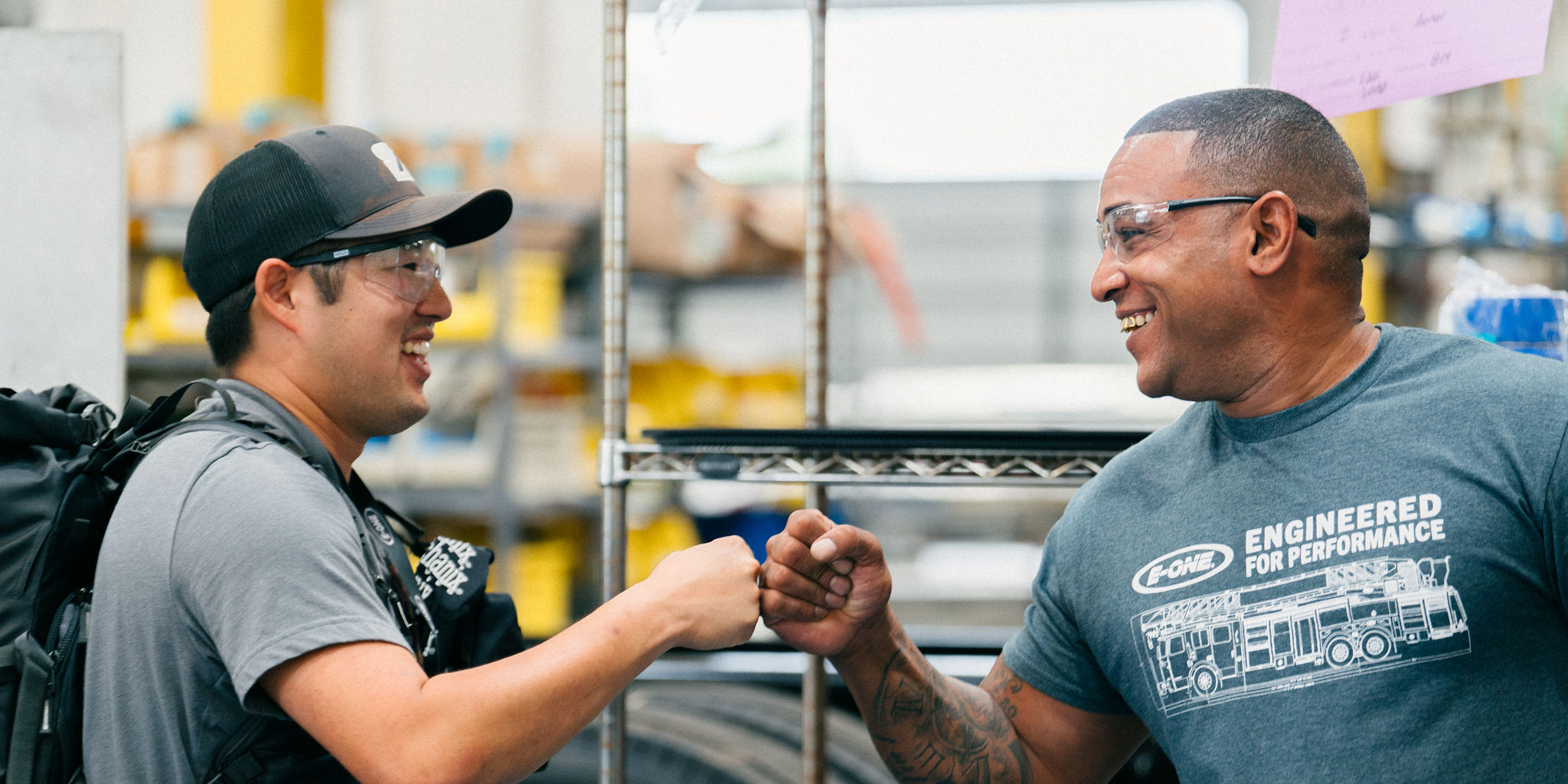 Two teammates share a fist bump on the E-ONE factory floor